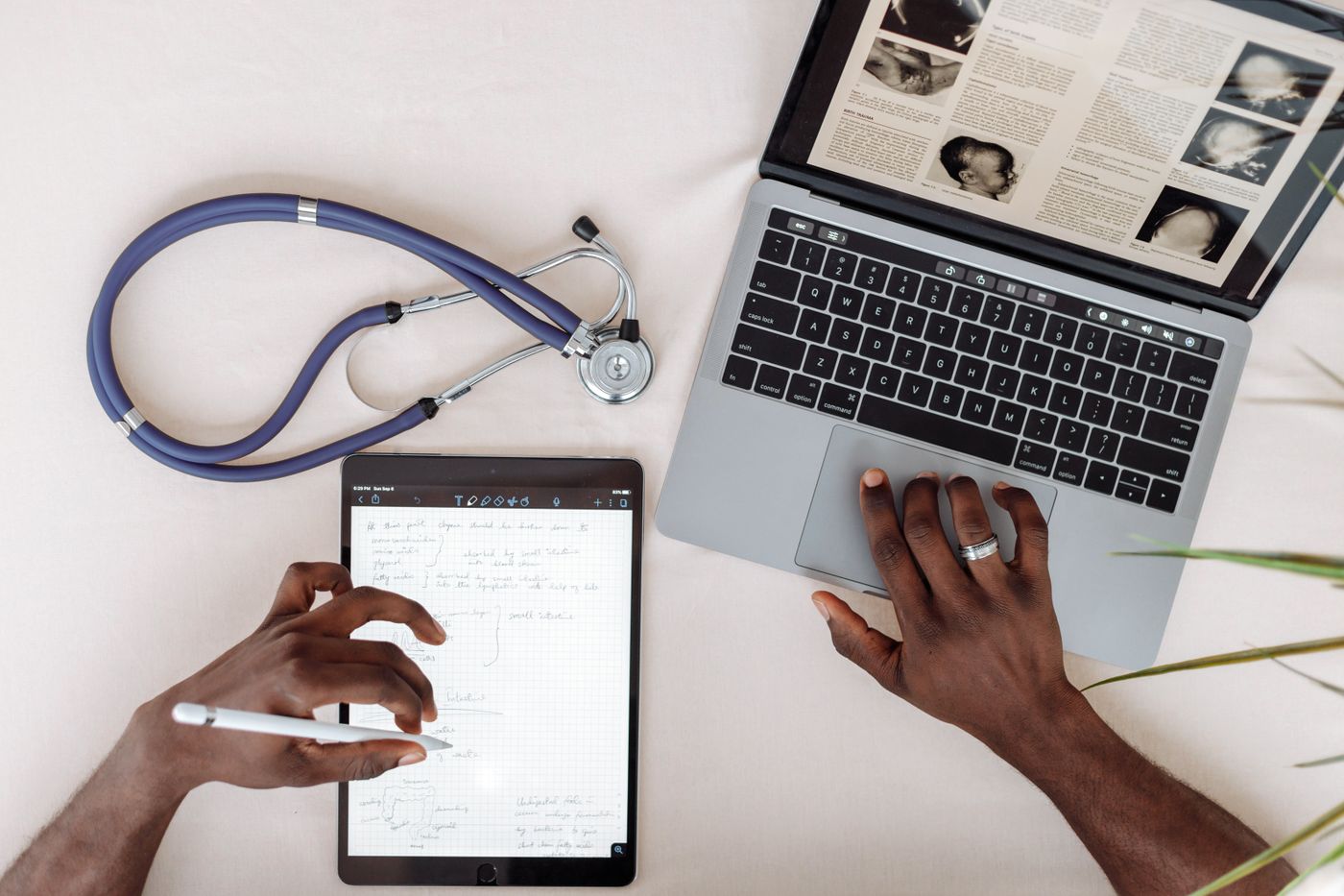 Healthcare provider reviewing patient notes on a tablet and laptop next to a stethoscope